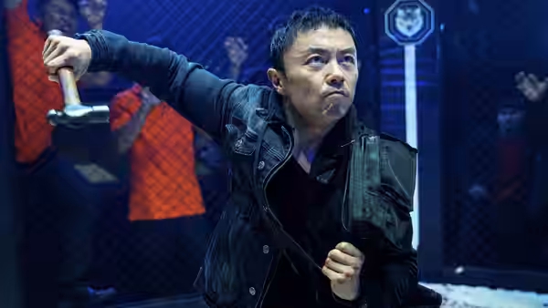 A man swings a hammer inside a chain link fighting cage