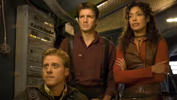 Mal Reynolds (Nathan Fillion) standing with Zoë Washburne (Gina Torres) and Wash (Alan Tudyk)