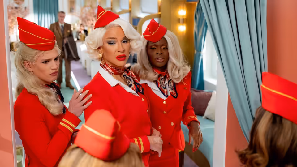 Three flight attendants in red uniforms stand together in a colorful lounge