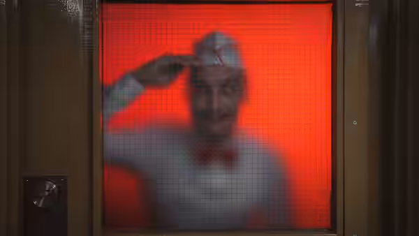 The Ice Cream Man (Ari Millen) salutes through a red lit service window