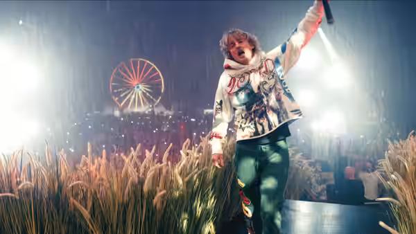 Hank (Owen Wilson) raises an arm onstage as a rain-soaked festival crowd cheers