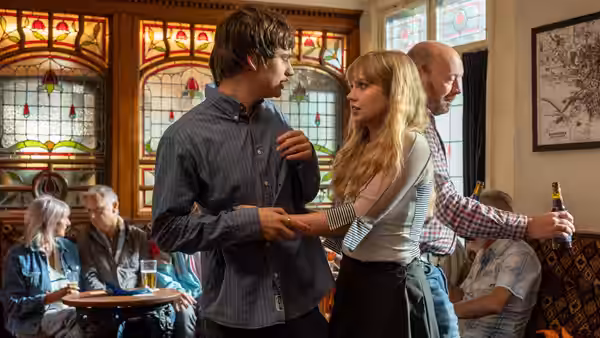 Owen (Spike Fearn) and Emily (Angourie Rice) talking in a pub as a man watches