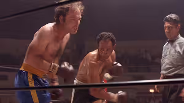 Ernie (Jeff Bridges) leans forward in the boxing ring beside his opponent and referee