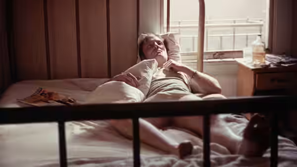 Tully (Stacy Keach) lies on a bed in a sunlit room