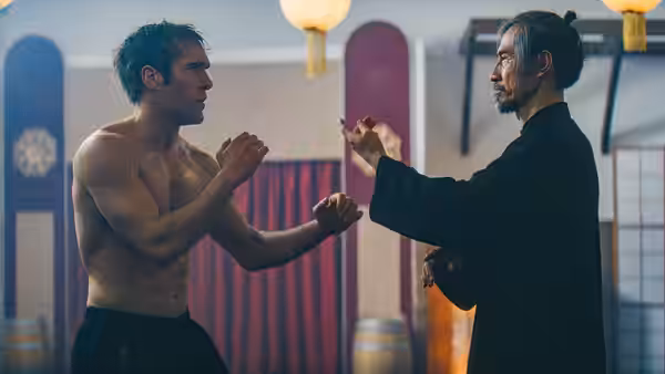 Shirtless man and older man in black robe facing off in fighting stances