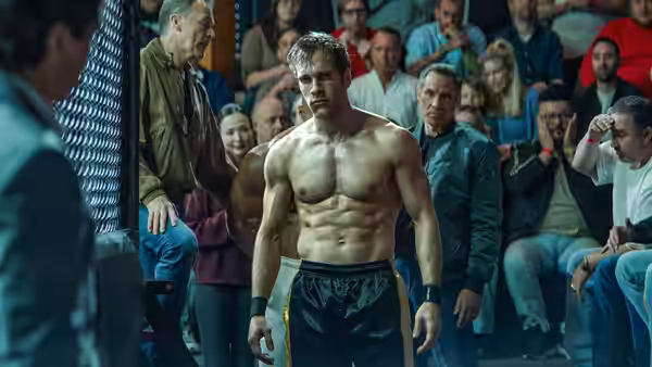 Shirtless muscular fighter with short hair standing before seated spectators