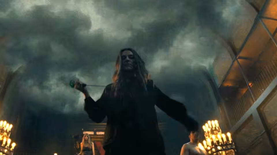 A long-haired figure stands beneath swirling smoke between glowing candlelit displays