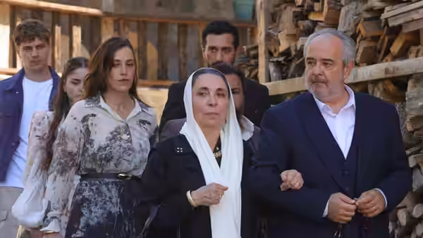 A headscarved woman and an older man stand with younger relatives beside a woodpile