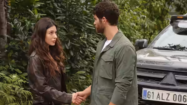 A woman and a man hold hands beside a parked vehicle in the woods