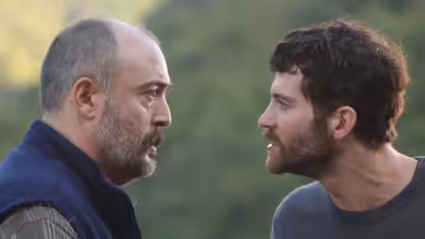 Two men confront each other face-to-face against a wooded hillside