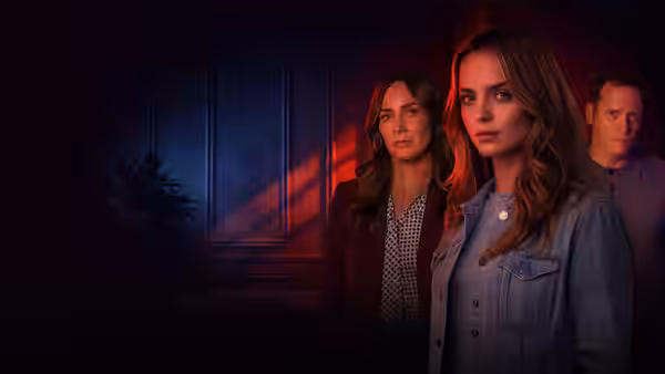Two women stand in foreground in dark room with red lighting, man behind