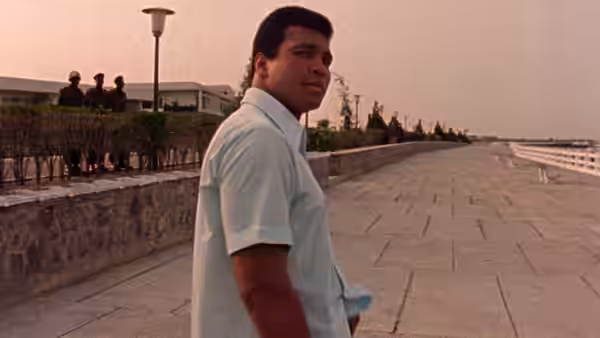 Muhammad Ali walking along a wide empty waterfront promenade