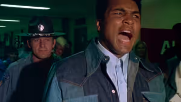 Muhammad Ali shouting while escorted through a crowded institutional hallway
