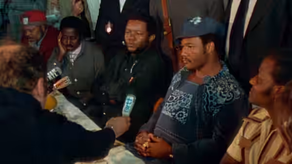Muhammad Ali seated at a table answering questions into a microphone