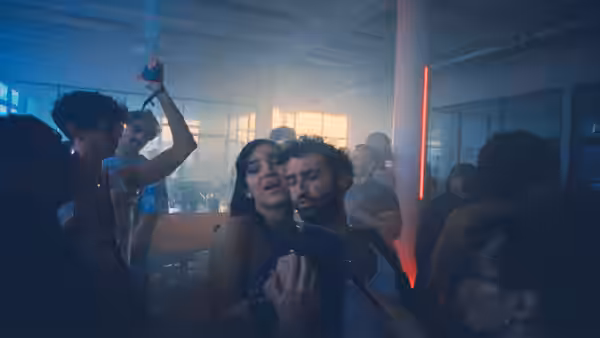 A man and woman dance among clubgoers beneath colored lights