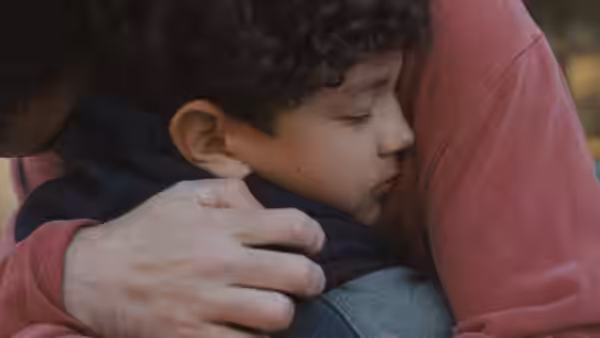 A curly-haired boy rests against an adult's chest as they embrace
