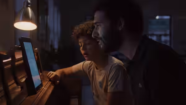 A man and boy sit together at a computer in a dim room