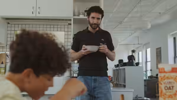 Peter (Jordan Firstman) holds a bowl while a boy eats at the kitchen counter