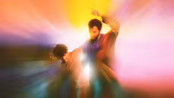 A bearded man and curly-haired boy dance beneath vivid, radiating lights