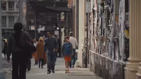 A man walks beside a young boy along a poster-covered city sidewalk