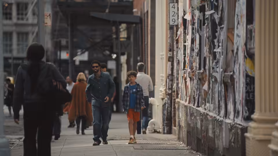 A man walks beside a young boy along a poster-covered city sidewalk