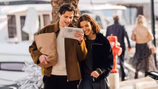 A young couple smile as they read a paper beside a marina