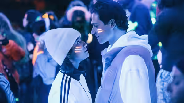 A young woman and man face each other amid a crowded party