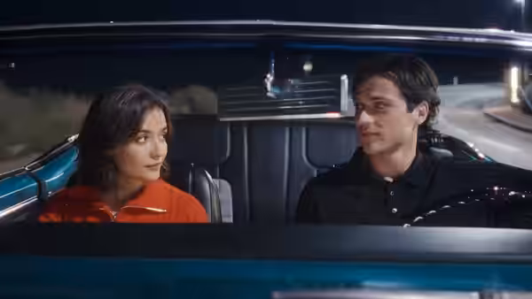A young woman and man sit together in a convertible at night