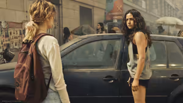 two women standing beside a blue car on a city street
