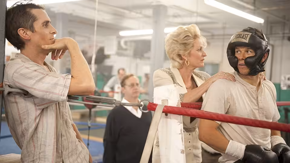Dicky Eklund (Christian Bale) leans on ropes while Alice Ward (Melissa Leo) stands with a boxer