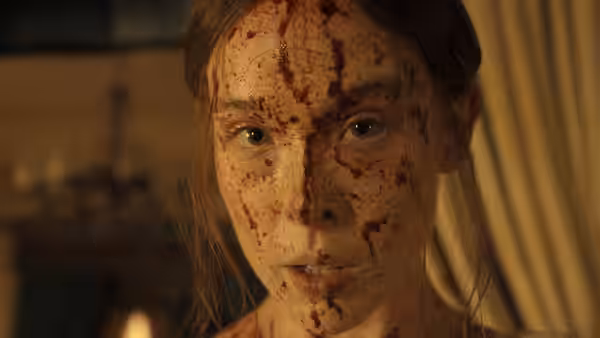 Young woman's blood-smeared face stares forward with wide eyes