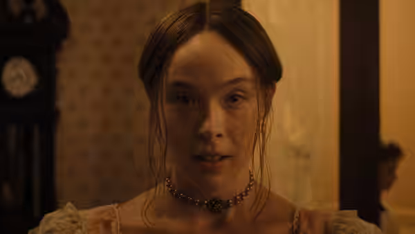 Wet-haired woman in pearl necklace gazes ahead in dim light