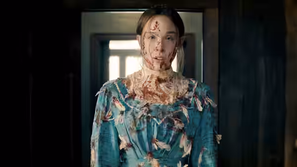 Bloodied woman in torn blue dress stands in a doorway