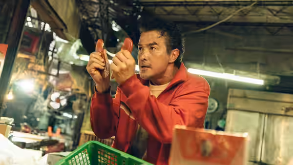a man in a red jacket examines two red items in a cluttered workshop