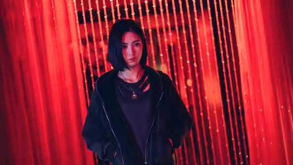 Mina Shen (Regina Lei) standing before red curtains in a dimly lit room