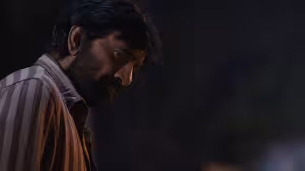 A bearded man in a striped shirt looks downward in the darkness