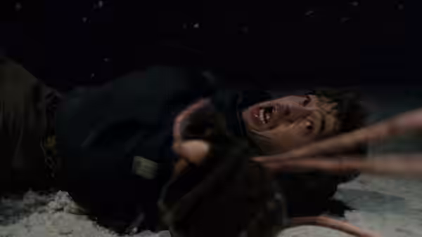 Man lies in snow reaching forward with mouth open in distress