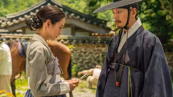 A woman studies a paper beside a traditionally dressed man in a courtyard
