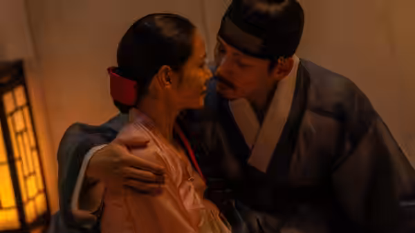 A man and woman in hanbok embrace closely in a dimly lit room