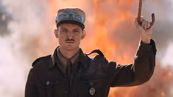 An officer in uniform raises a metal hook before a fiery explosion