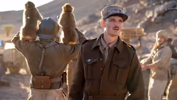 Two soldiers stand in a desert as one holds boots overhead