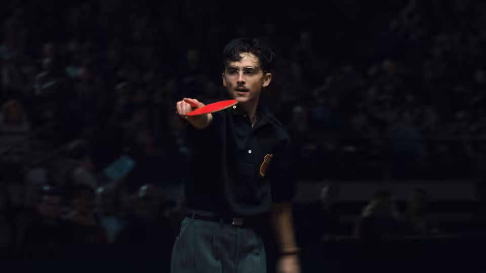 Marty Mauser (Timothée Chalamet) holding a red paddle in a large arena