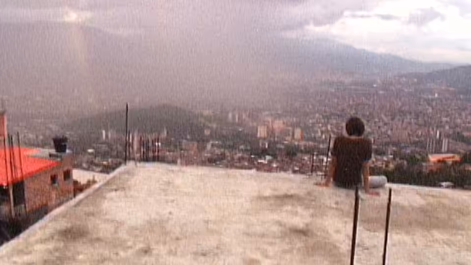 A young man sits on a rooftop overlooking a sprawling city at dusk