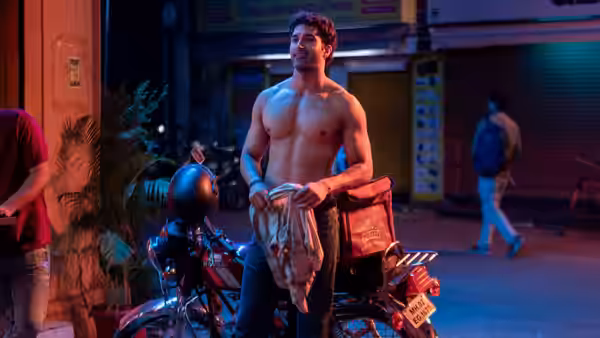 A shirtless man holding a garment beside a motorcycle on a street at night