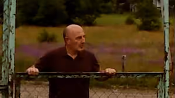 Irakli (David Koberidze) leaning on a green metal gate in the countryside