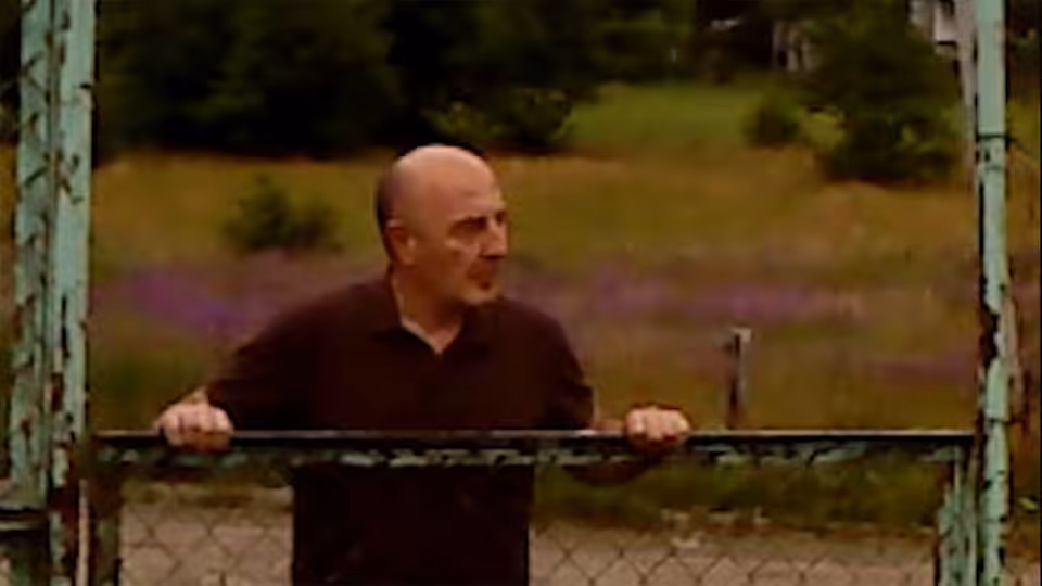 Irakli (David Koberidze) leaning on a green metal gate in the countryside