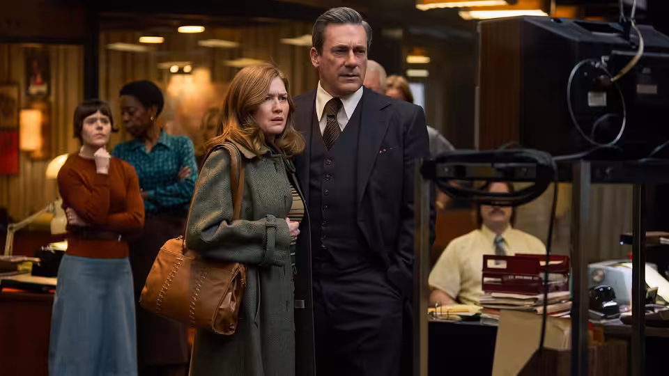 Fred Heckman (Jon Hamm) and Barbara Heckman (Mireille Enos) standing in a newsroom