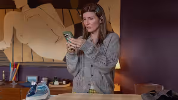 Sharon Horgan looks at her phone while standing in a domestic room