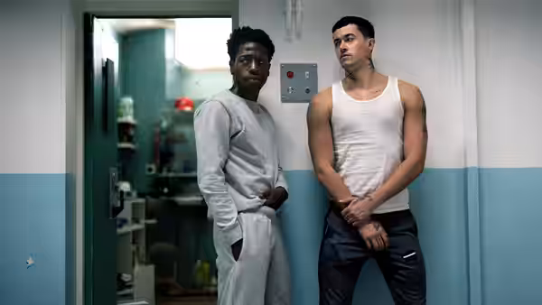 Two men standing side by side against a corridor wall