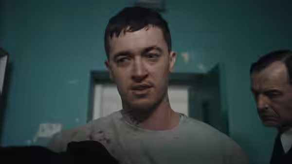 A bloodied man with a neck tattoo standing beside a suited man